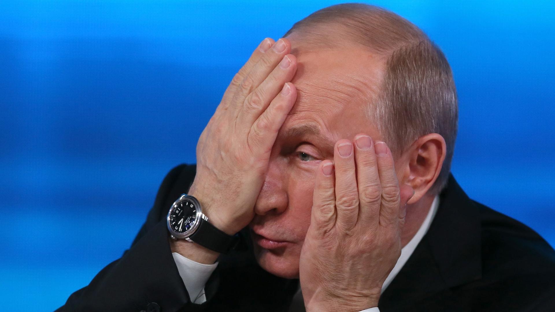 Der russische Präsident Wladimir Putin hält sich eine Hand vor sein Gesicht.