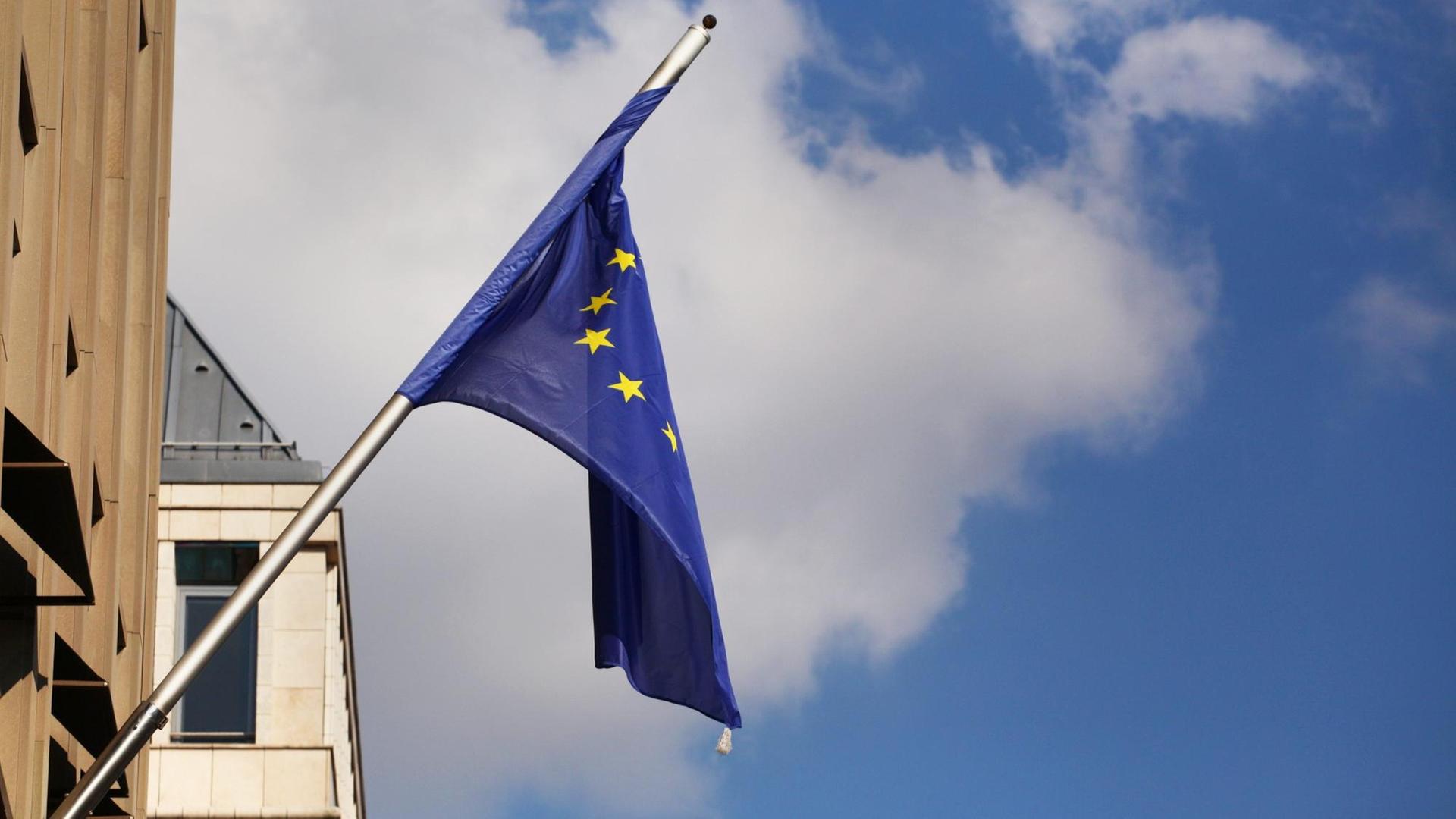 Schlapp und verdreht hängt eine Europafahne an einem Gebäude.