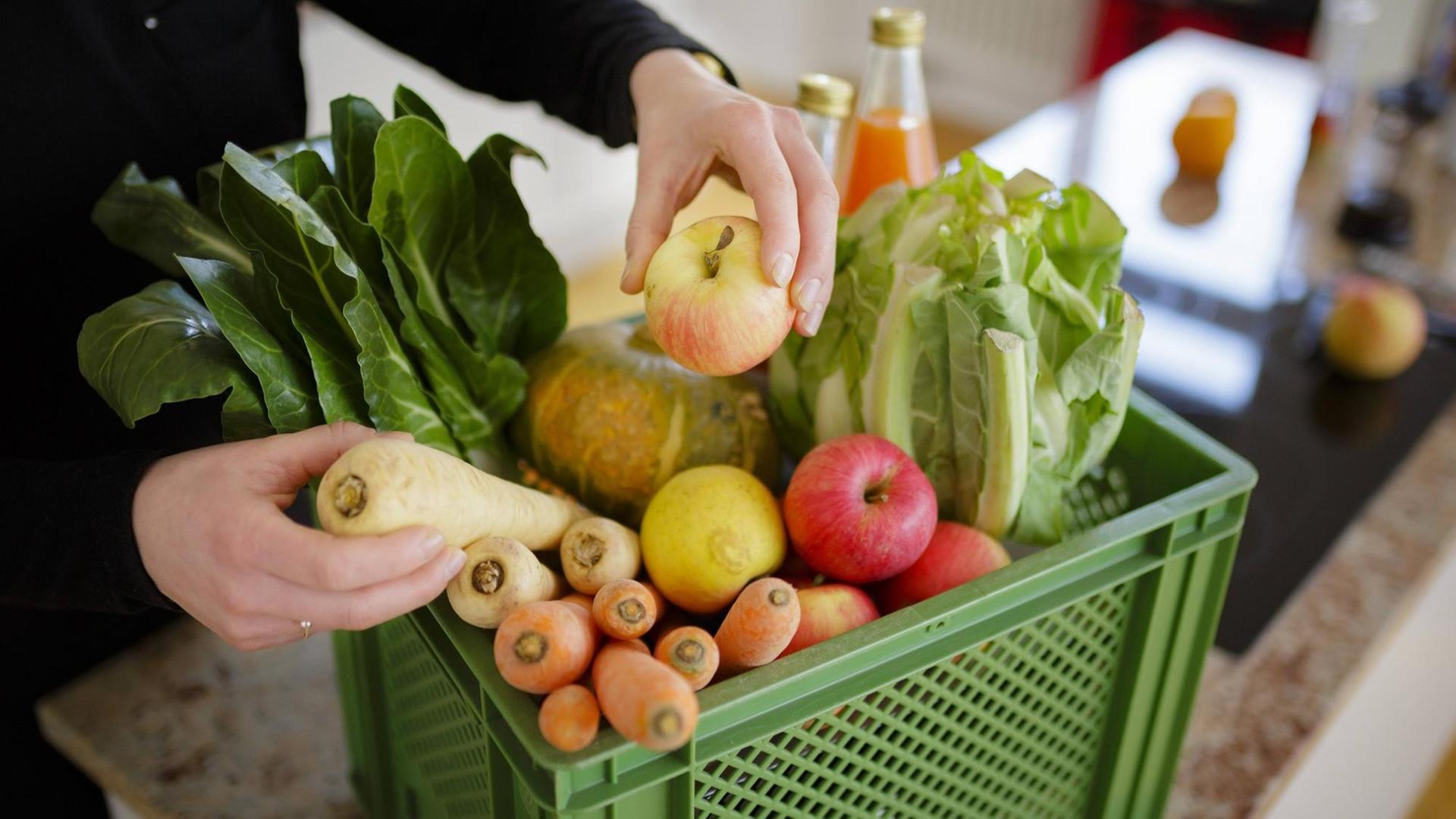 Die Hände einer Frau mit einer Biokiste mit Obst und Gemüse.