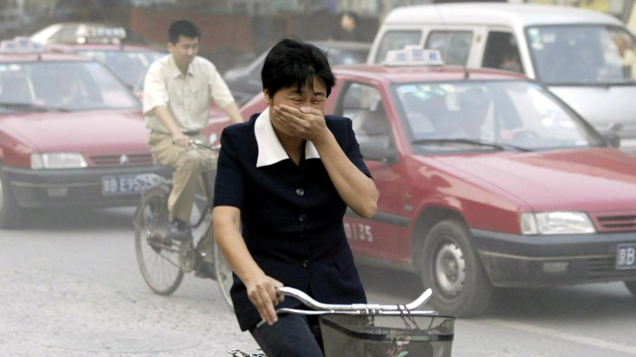 Eine Fahrradfahrerin hält sich in einer Hauptverkehrsstraße in Peking wegen des Smogs eine Hand vor Mund und Nase.