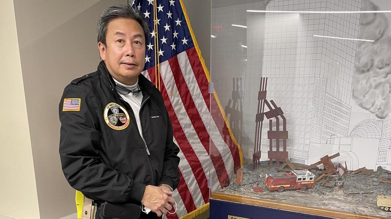 Der New Yorker Arzt Gordon Huie steht in einer schwarzen Uniform vor einer US-amerikanischen Flagge, neben ihm in einer Vitrine sind Gegenstände zu sehen, die an die Anschläge vom 11. September 2001 erinnern.