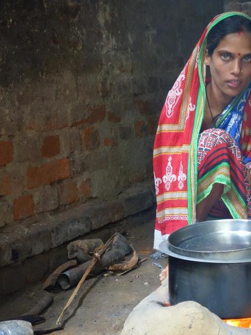 In den Dörfern des ärmsten indischen Bundesstaates Odisha kochen viele Familien auf offenem Feuer im Wohnhaus. Hier sitzt eine Frau am Kochtopf auf dem Boden, dahinter ein Kind.
