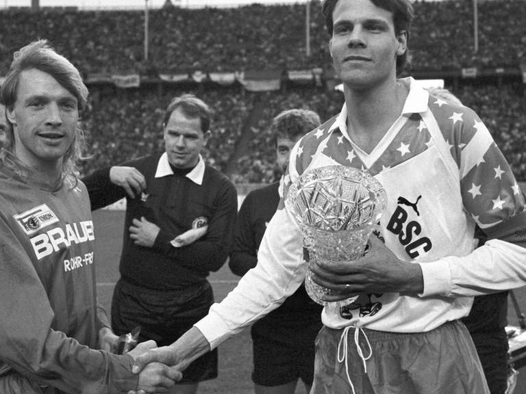 Die beiden Mannschaftskapitäne geben sich vor Beginn des innerstädtischen "Fußball-Gipfels" zwischen Hertha BSC und Union Berlin am 27.01.1990 im Olympiastadion in Berlin die Hand.