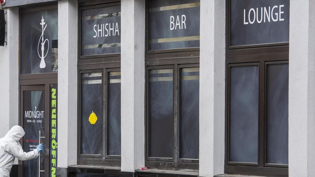 Ein Polizist in weißer Schutz-Kleidung betritt das Lokal. Über dem Eingang steht "Shisha Bar Lounge".