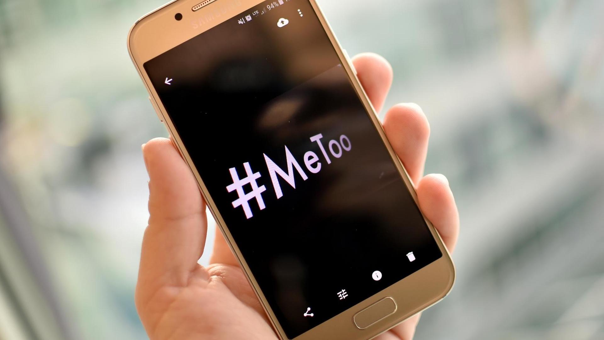Eine junge Frau hält ein Smartphone mit dem Hashtag "#MeToo" in der Hand