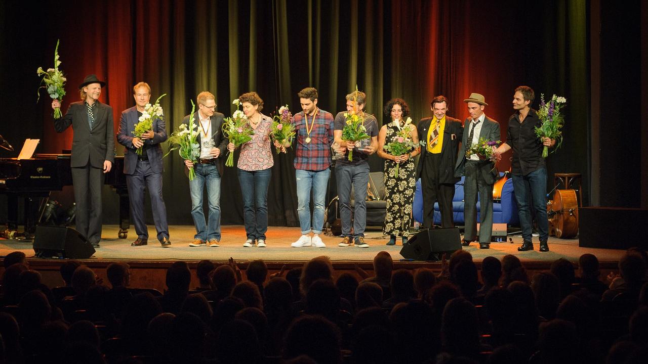 Alle Teilnehmer (10 Personen)des Saisonfinales gemeinsam auf der Bühne, sie halten jeweils einen gelb-grünen Blumenstrauß in der Hand.