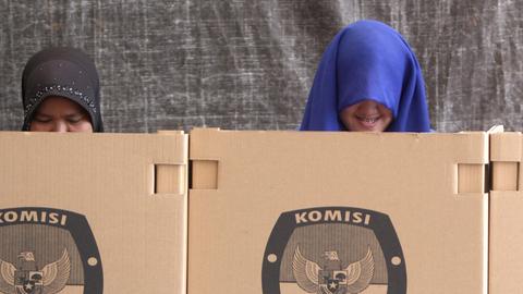 Zwei Frauen wählen in Indonesien in Kabinen aus Pappe.