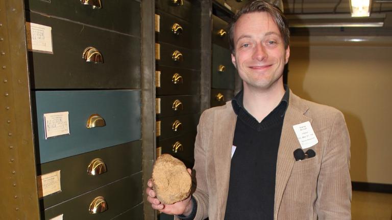 DLF-Reporter Michael Stang hält in der Sammlung des National Museum of Natural History in Washington einen Koprolithen in der Hand und grinst.