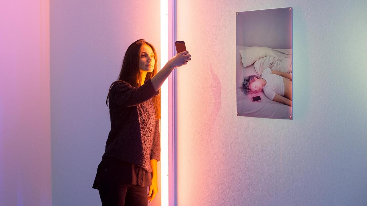 Eine Frau macht in der Ausstellung ein Selfie vor einem Bild an einer Wand