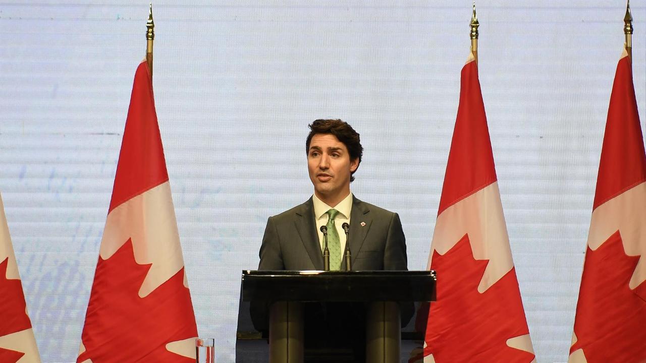 Kanadas Premier-Minister Justin Trudeau steht an einem Redner-Pult. Im Hintergrund sind Kanada-Flaggen.