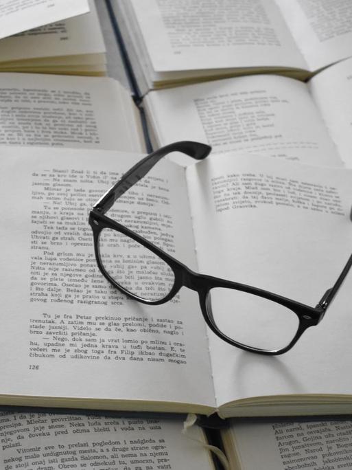 Eine schwarze Brille liegt auf einem Stapel aufgeschlagener Bücher.