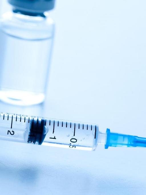 Injektionsnadeln und Ampullen mit Impfstoff liegen auf einem Tisch.