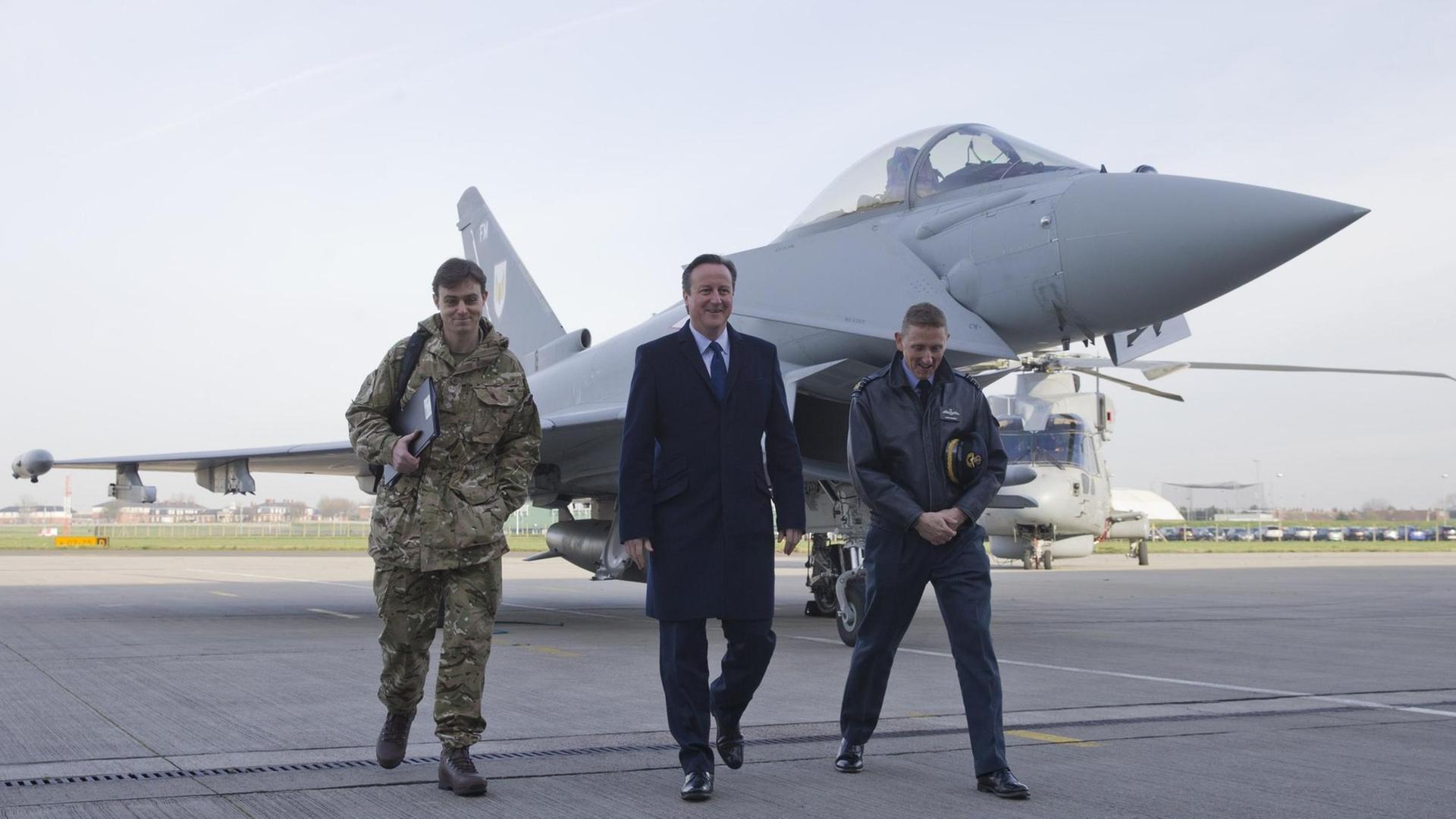 David Cameron und zwei britische Soldaten laufen vor einem Kampfjet über das Rollfeld