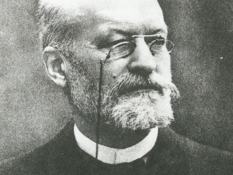Eine schwarz-weiße Fotografie zeigt Er war den französischen Mediziner und Bakteriologen Charles Louis Alphonse Laveran. Er trägt einen graue Vollbart und randlose Brille.