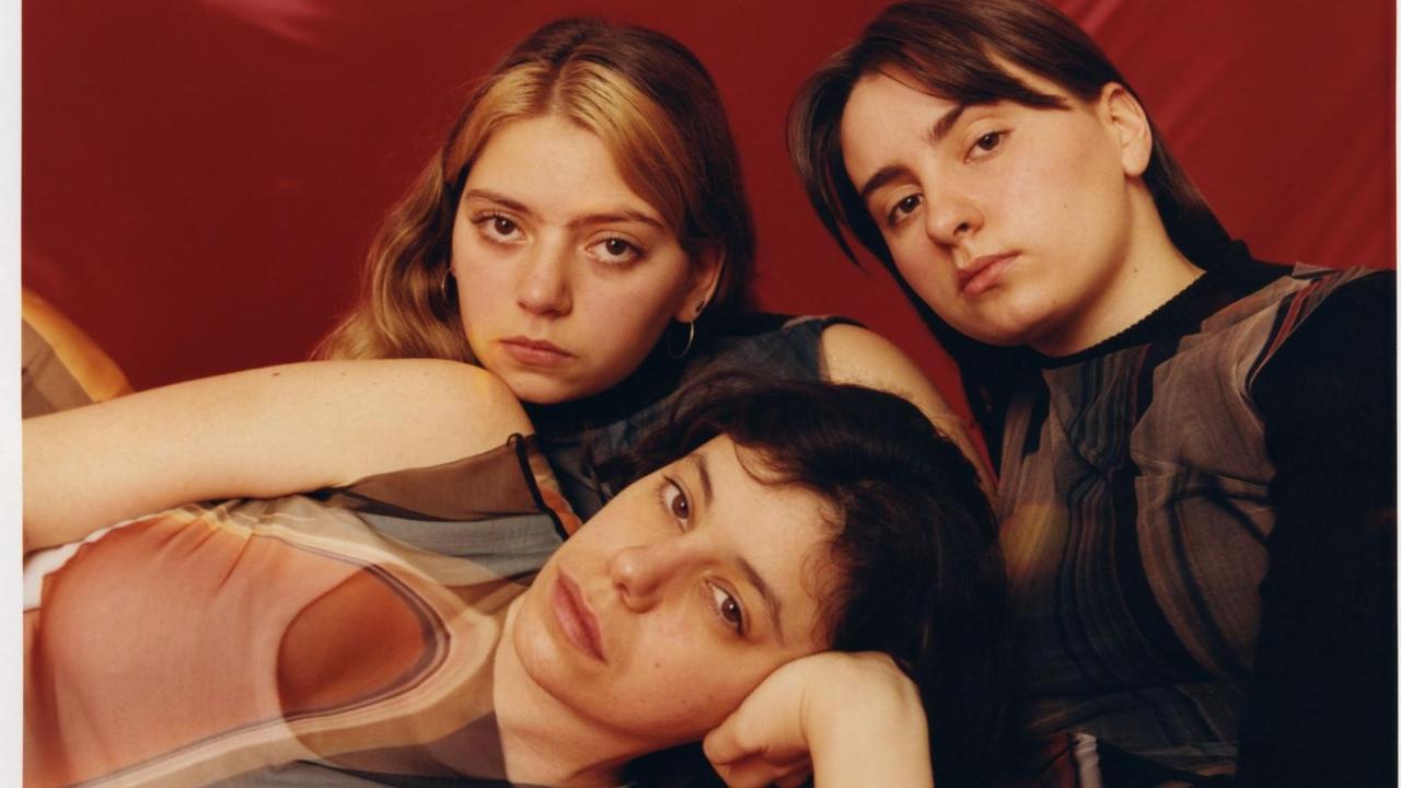 Drei Frauen liegen nebeneinander auf einer roten Decke. Die vordere Frau stützt ihren Kopf auf ihre Hand.