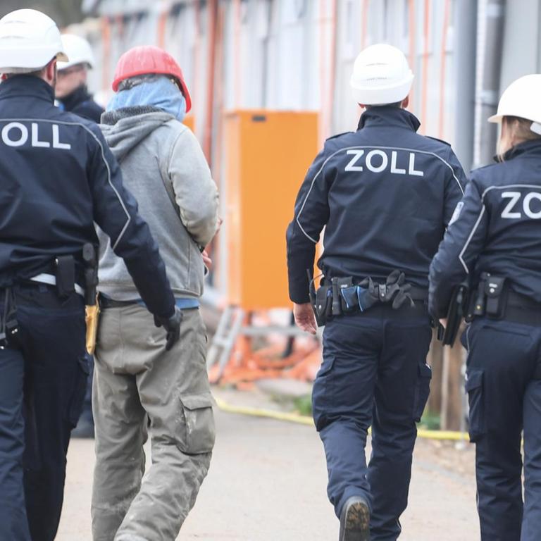 Beamte des Zoll kontrollieren einen Bauarbeiter während eines Einsatzes auf einer Großbaustelle in Frankfurt.
