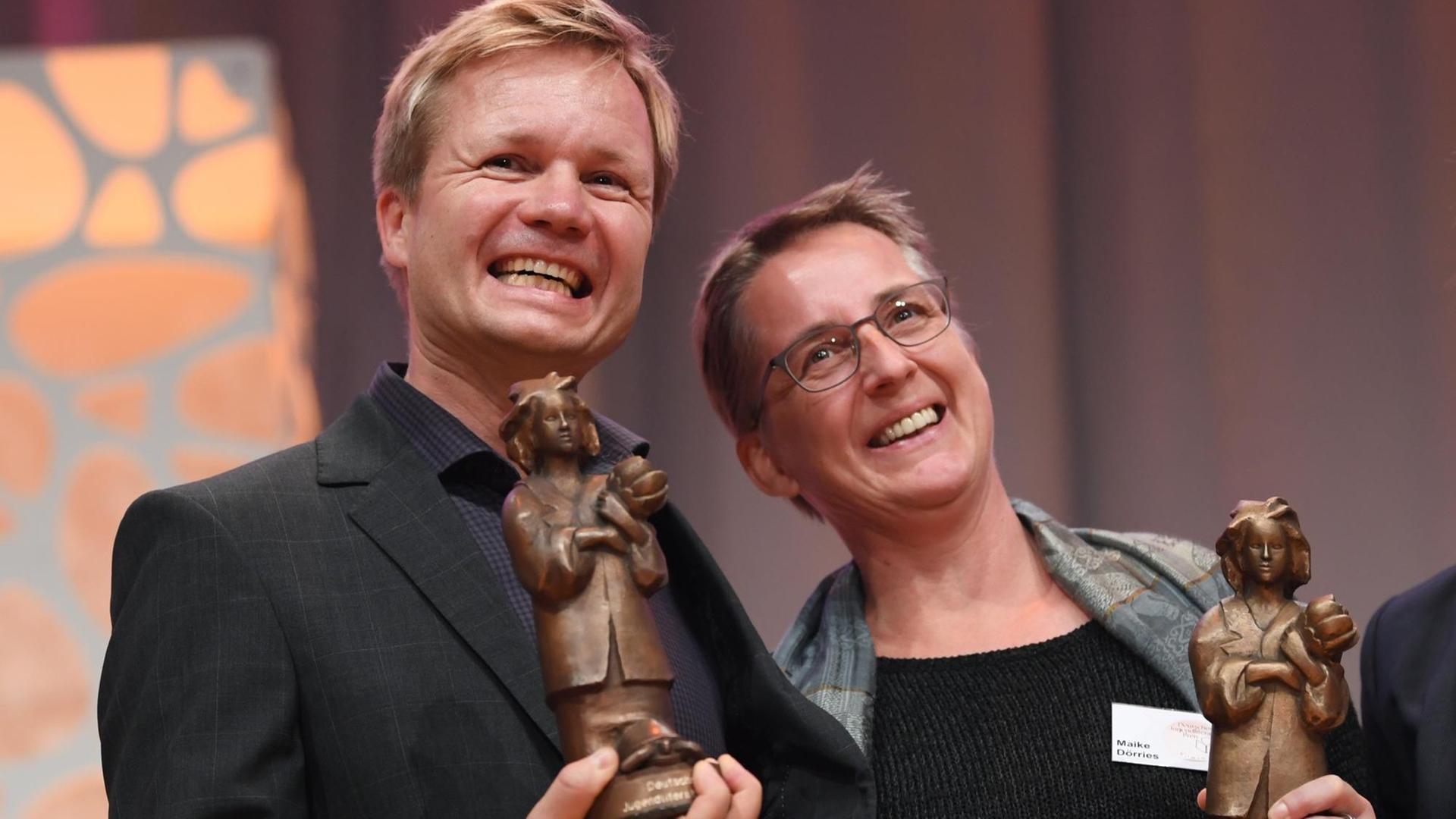 Der Autor und Illustrator Oyvind Torseter aus Norwegen und die Übersetzerin Maike Dörries halten auf der Frankfurter Buchmesse während der Verleihung des Deutschen Jugendliteraturpreises 2018 die Momo-Trophäen in Händen
