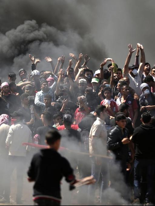 Palästinensische Demonstranten protestieren nahe der Grenze zwischen Gaza und Israel, im Hintergrund brennen Autoreifen.