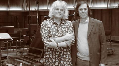 Schwarz-Weiß Fotografie Ronald Brautigam (links) und Michael Alexander Willens (rechts) haben schon in Koproduktion mit BIS Records u.a. alle Konzerte von Mozart, Mendelssohn und Beethoven im Dlf Kammermusiksaal aufgenommen. Beide stehen vor einen historischen Flügel im Dlf Kammermusiksaal. R. Brautigam trägt ein geblümtes Hemd, M.A. Willens einen hellen Pullover und darüber ein graues Sakko