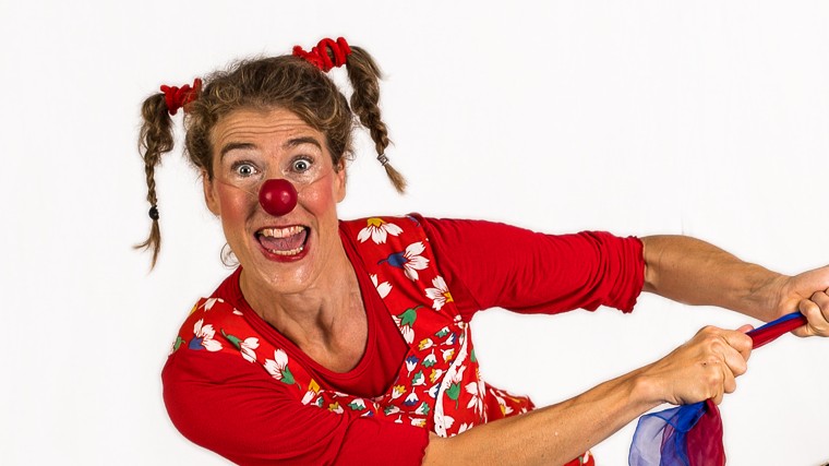 Ein weiblicher Clown zieht an einem Tuch und lacht.