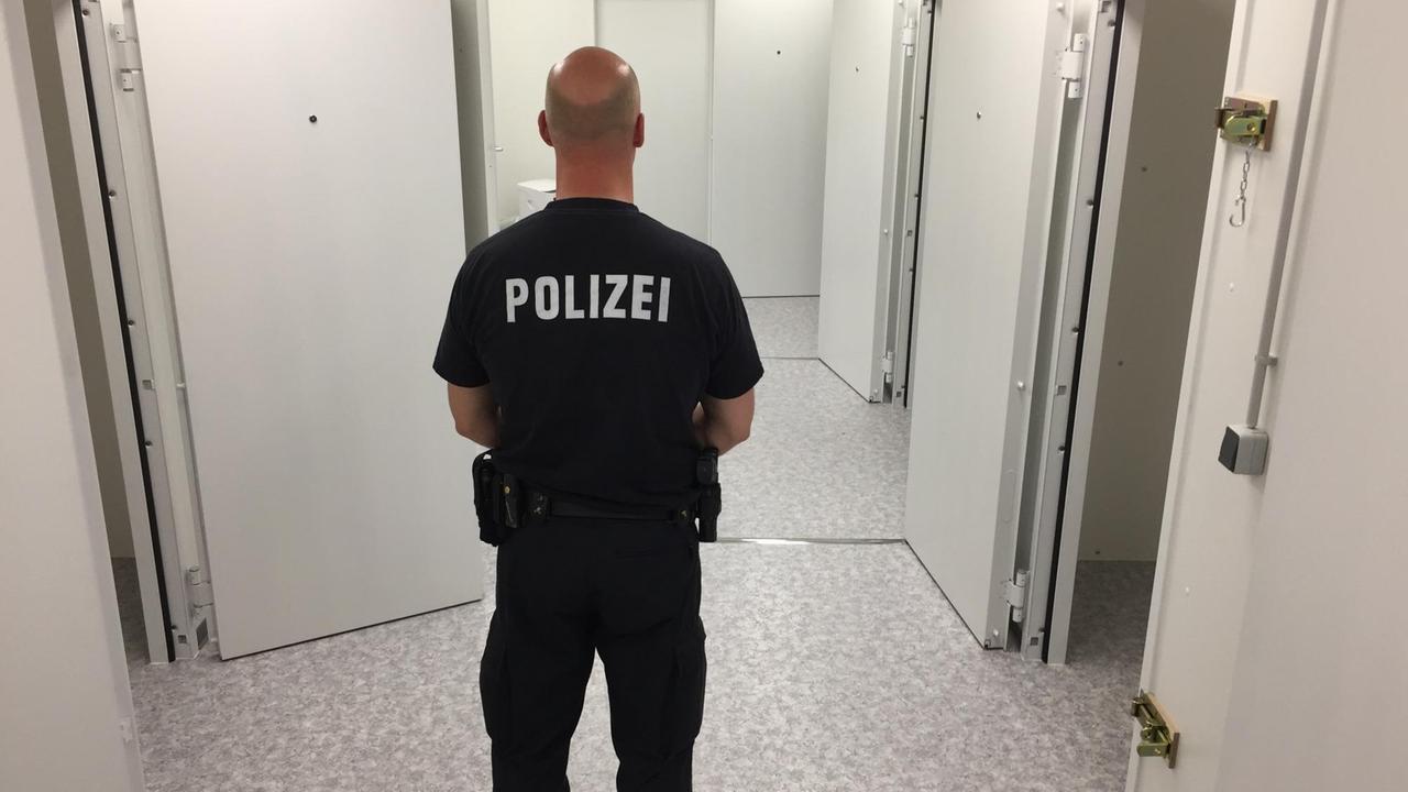Polizist in Rückansicht vor geöffneten Arrestzellen