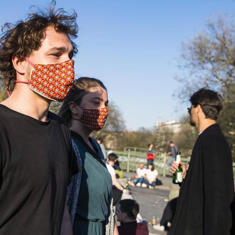 Ein junger Mann und eine junge Frau tragen selbstgemachte bunte Mundschutzmasken. Ihnen kommen ein Mann und eine Frau ohne Mundschutzmaske entgegen.
