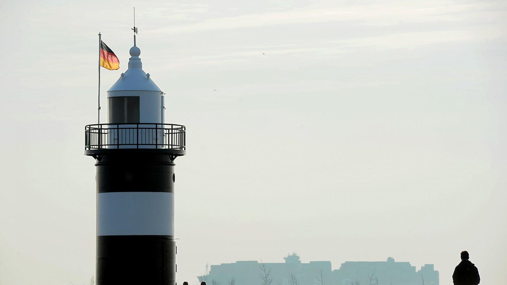 Nordseebesucher genießen am kleinen, schwarzweissen Leuchtturm an der Sielhafeneinfahrt von Wremen (Niedersachsen) am 17.03.2015 das frühlingshafte Wetter an der Aussenweser, während ein Mega-Containerschiff mit Kurs Bremerhaven vorbeifährt. Bei Sonnenschein und Temperaturen um die zwölf Grad Celsius liegt zur Zeit ein wenig Frühling in der salzigen Nordseeluft.