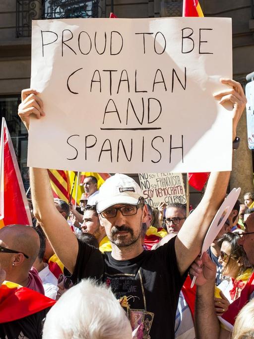 Ein Mann hält in einer Menschenmenge ein Plakat mit der Aufschrift "Stolz, Katalane und Spanier zu sein" in die Höhe.