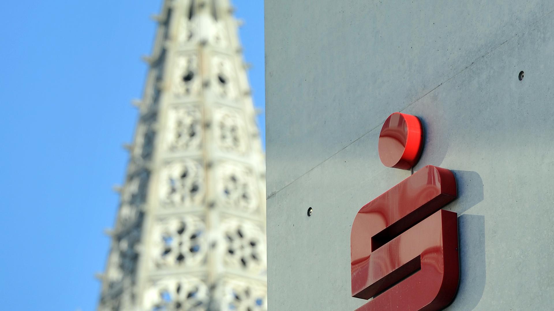 Das Logo der Sparkasse Ulm an einem Gebäude, im Hintergrund das Ulmer Münster.