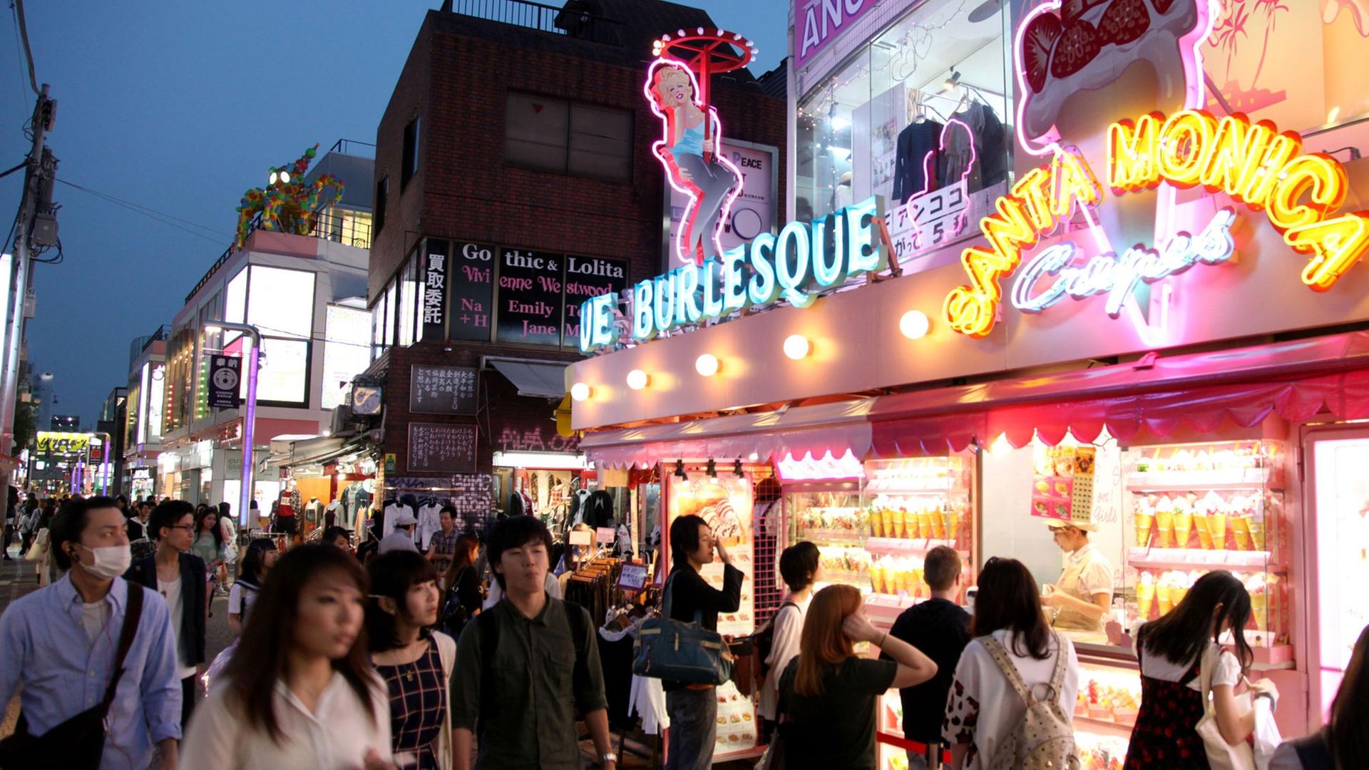 Passanten laufen durch eine Einkaufsstraße mit greller Leuchtreklame an den Geschäften in der japanischen Hauptstadt Tokio.