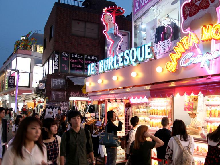 Passanten laufen durch eine Einkaufsstraße mit greller Leuchtreklame an den Geschäften in der japanischen Hauptstadt Tokio.