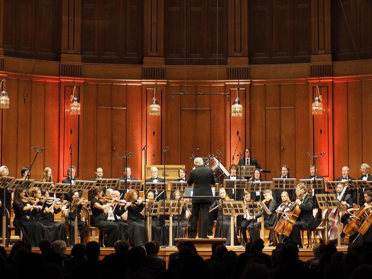 Ein Streichorchester sitzt auf der Bühne, dahinter rundherum ein Chor.