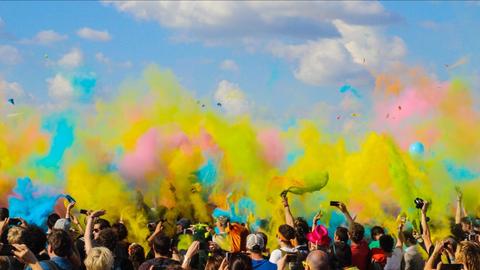 Tanzende Menschen vor blauem Himmel in dem sich buntes Puder verteilt.