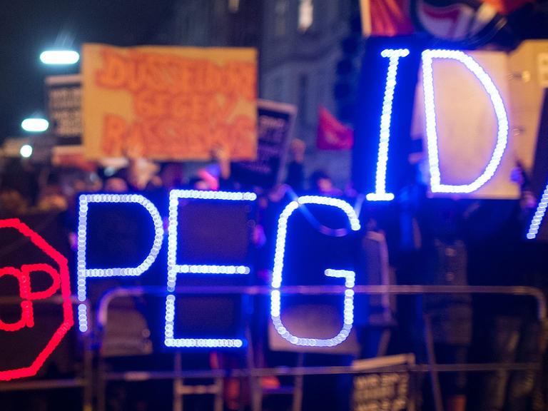 Gegner der Anti-Islam-Bewegung "Dügida" demonstrieren am 12.01.2015 in Düsseldorf (Nordrhein-Westfalen) mit einer Leuchtschrift "Stop PEGIDA"