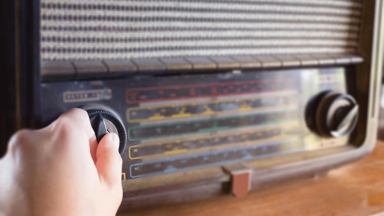 Eine Hand an einem alten Radio wählt ein Programm aus. 