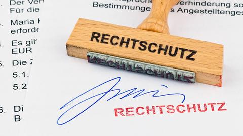 Ein Stempel aus Holz liegt auf einem Dokument. Aufschrift: Rechtschutz