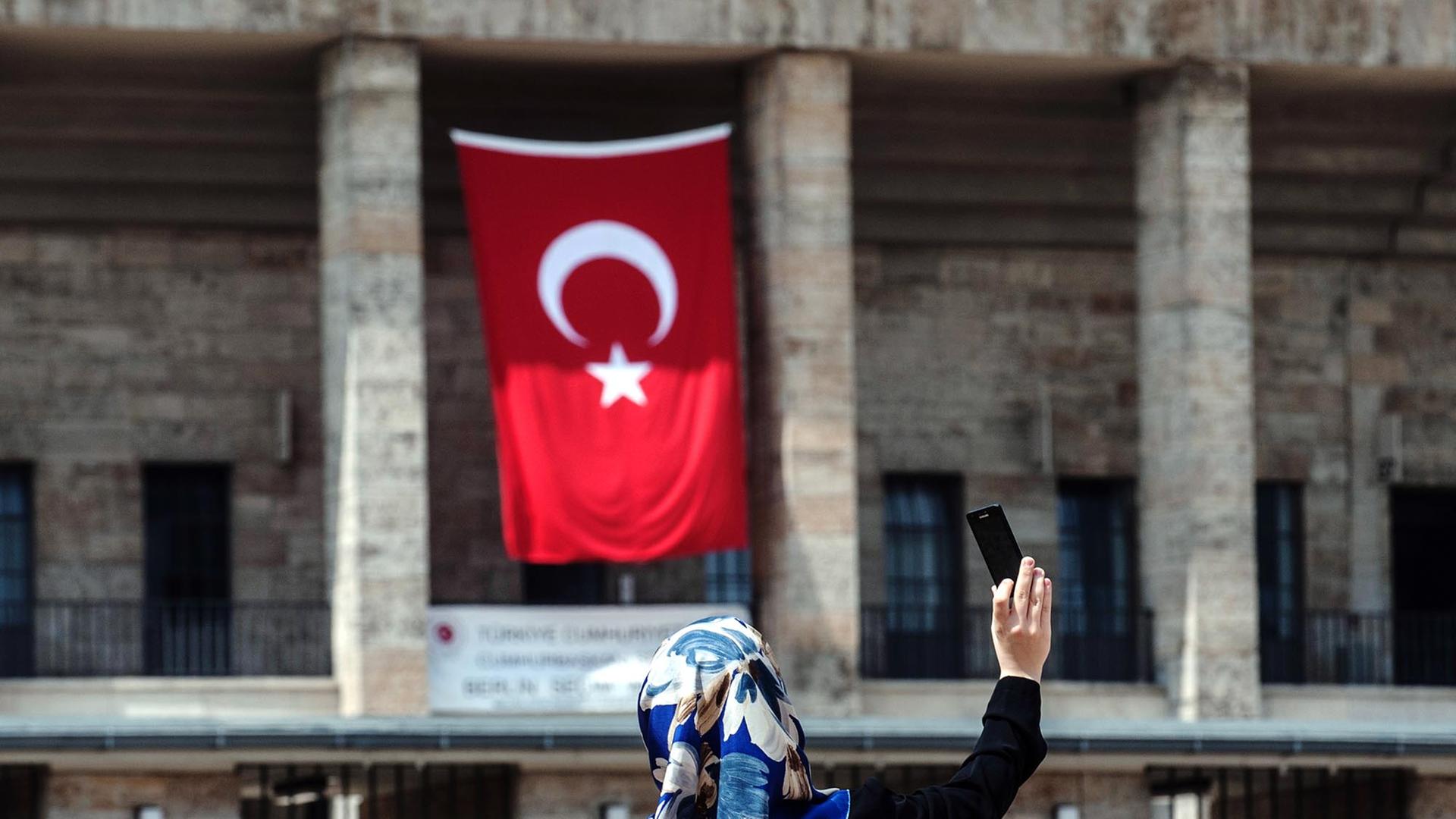 Eine Frau mit Kopftuch fotografiert sich selbst am 03.08.2014 vor dem Olympiastadion in Berlin, an dem eine türkische Fahne hängt. Im Olympiastadion ist ein Wahlzentrum für die türkische Präsidentenwahl in Deutschland. Erstmals können türkische Staatsangehörige in Deutschland an der türkischen Präsidentenwahl teilnehmen.