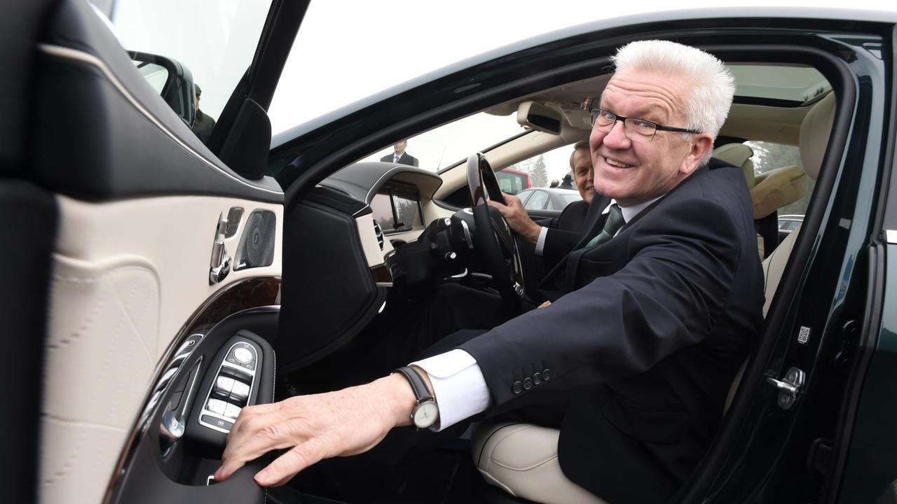 Winfried Kretschmann posiert auf dem Fahrersitz eines Autos.