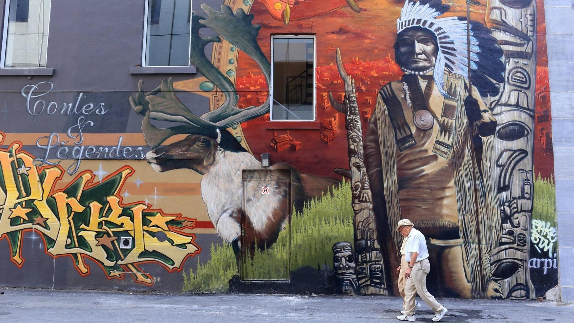 Ein Mann läuft an einer Häuserwand mit einem mit einem Ureinwohnermotiv vorbei