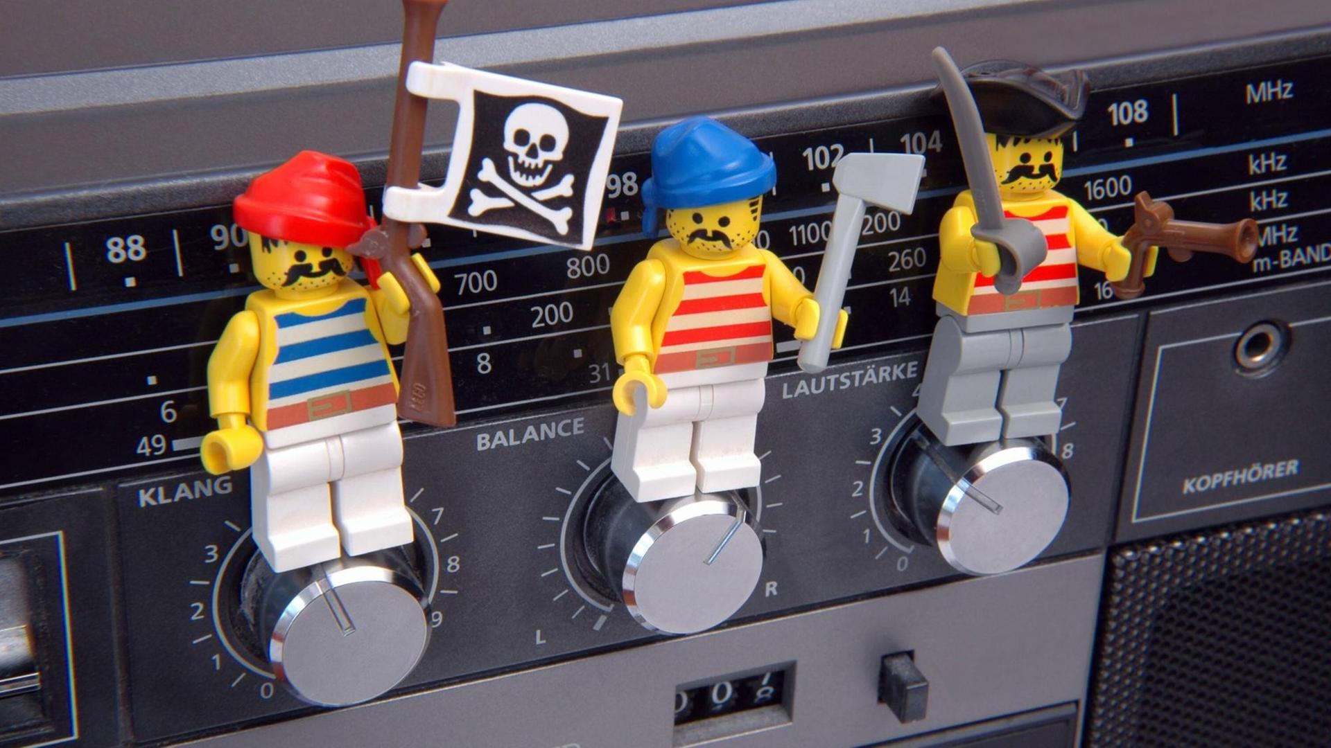 Drei Playmobilfiguren stehen auf Drehknöpfen eines Radios.