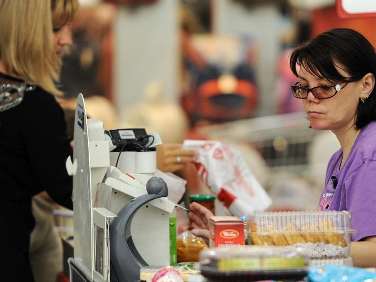 Eine Frau steht zum Bezahlen in einem Supermarkt an der Kasse.