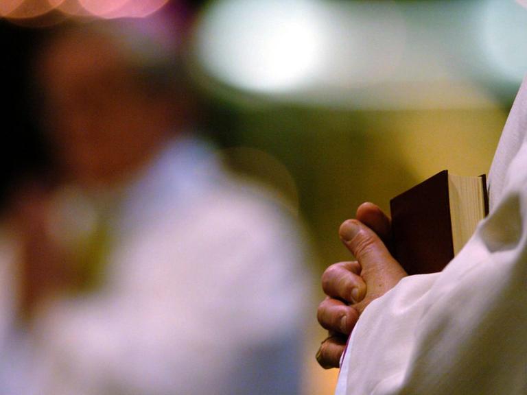Bischöfe und Priester sitzen mit Gesangbüchern und Bibeln in der Hand im Kölner Dom.