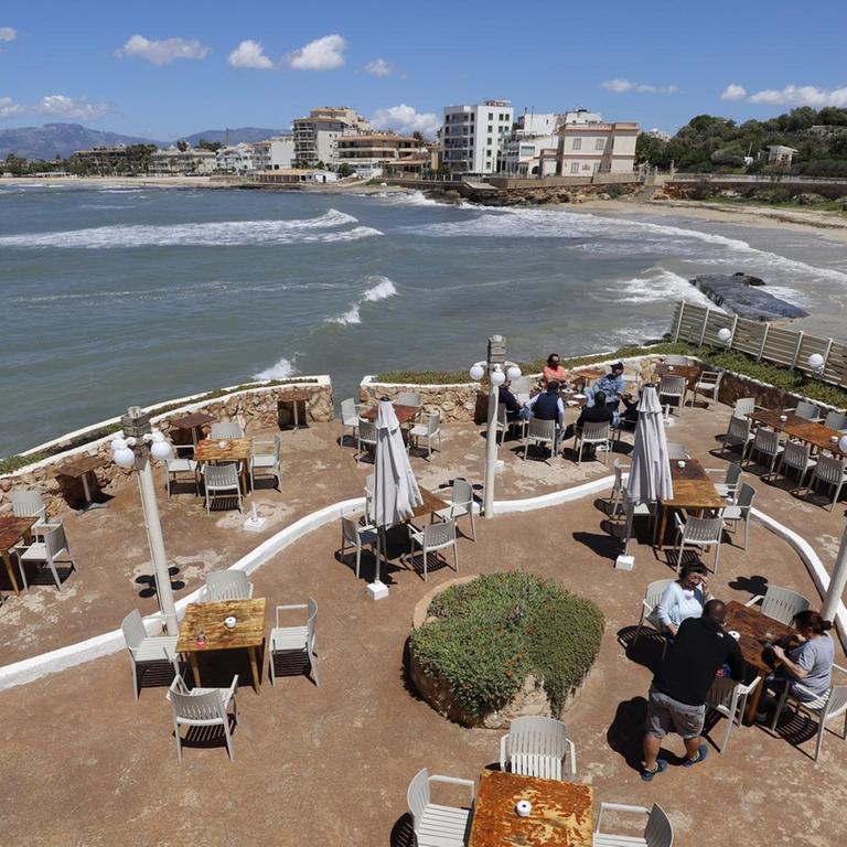 Menschen sitzen auf der Terrasse der Bar El Pe-on am Meer, Spanien.