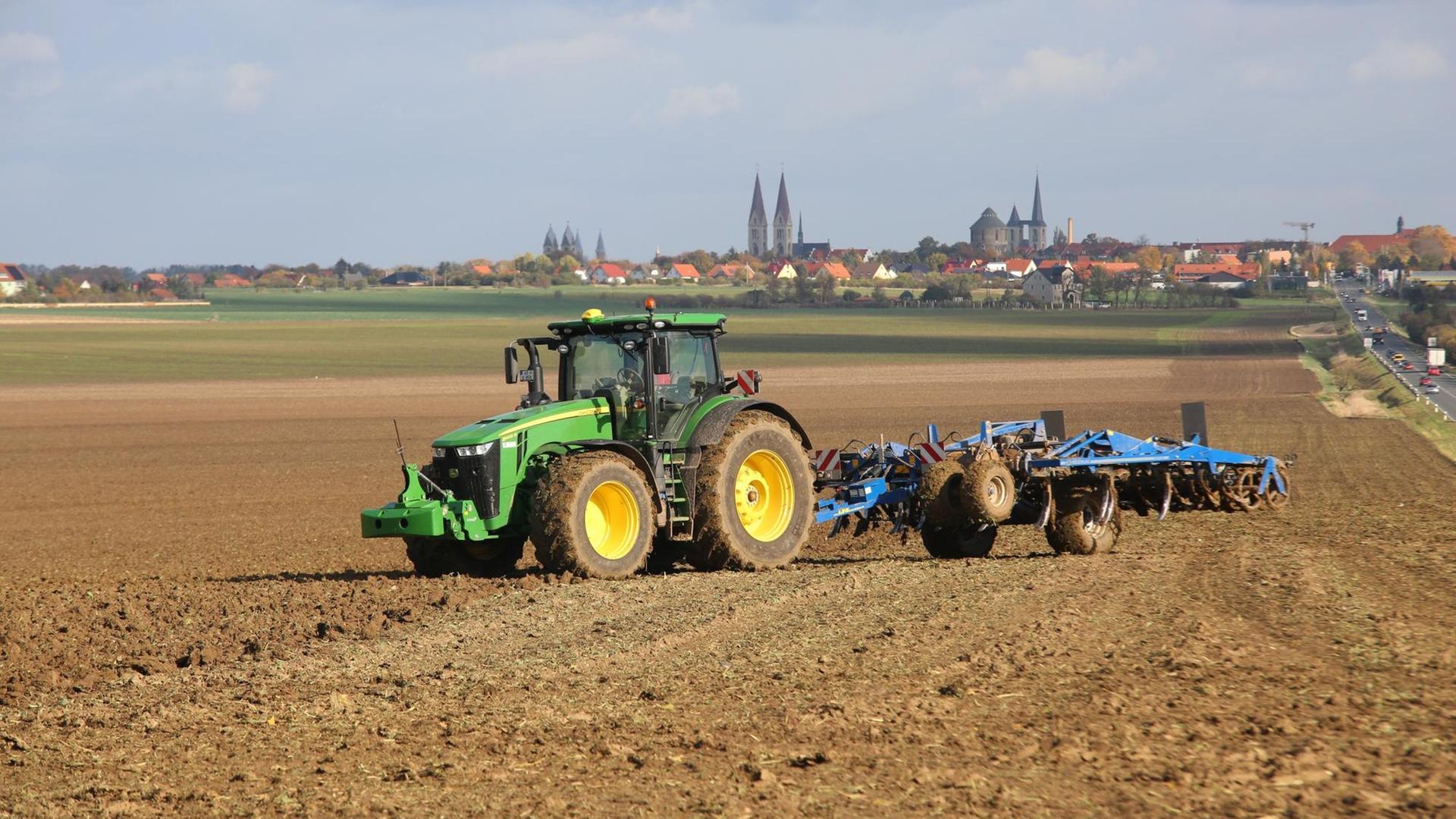 Ein Landwirt pflügt mit einem Traktor ein abgeerntetes Feld. Im Hintergrund ist eine Stadt zu sehen. Ein Landwirt pflügt mit einem Traktor ein abgeerntetes Feld. Im Hintergrund ist eine Stadt zu sehen.