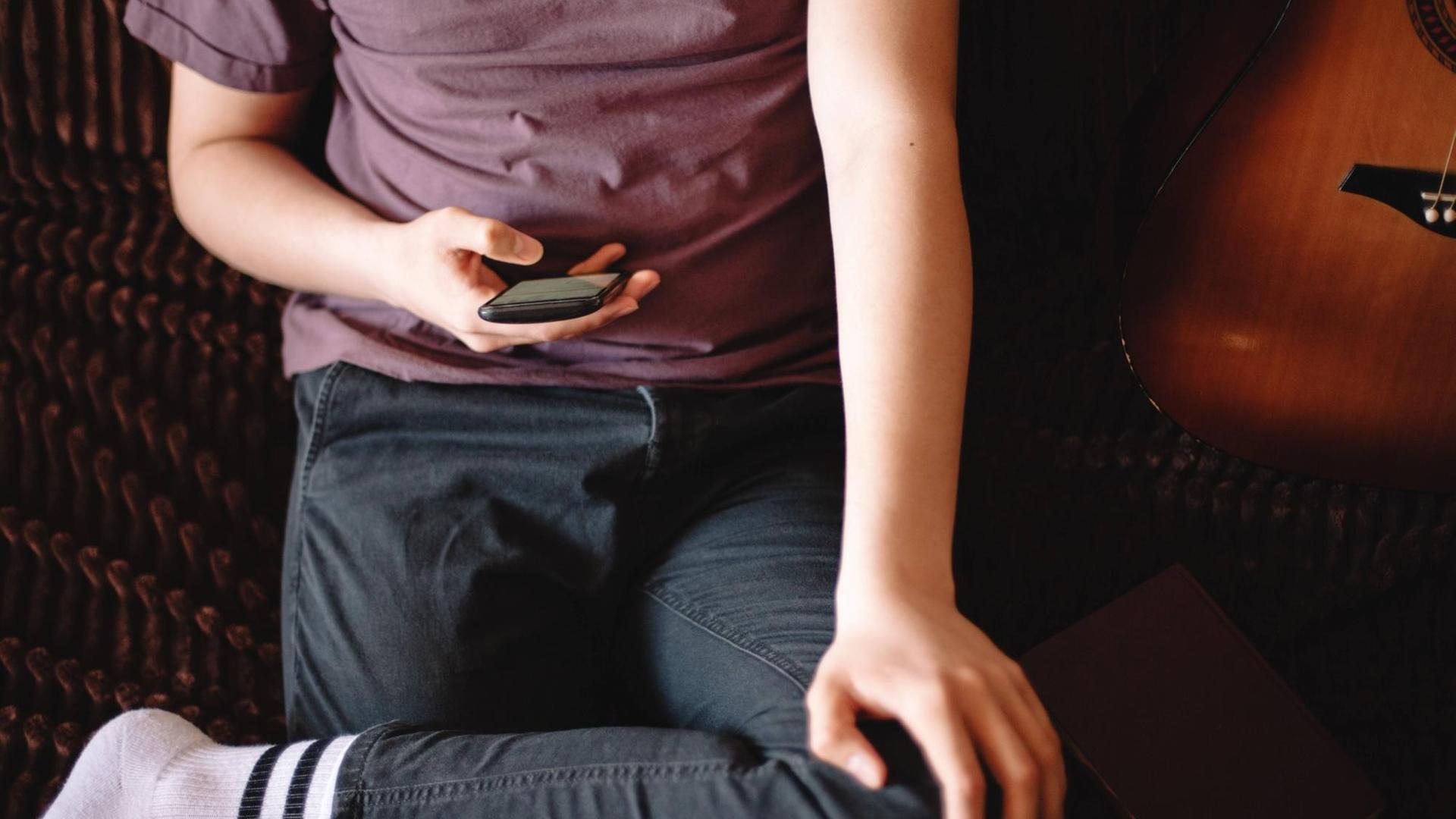 Ein Jugendlicher sitzt auf einem Sofa und benutzt ein Smartphone