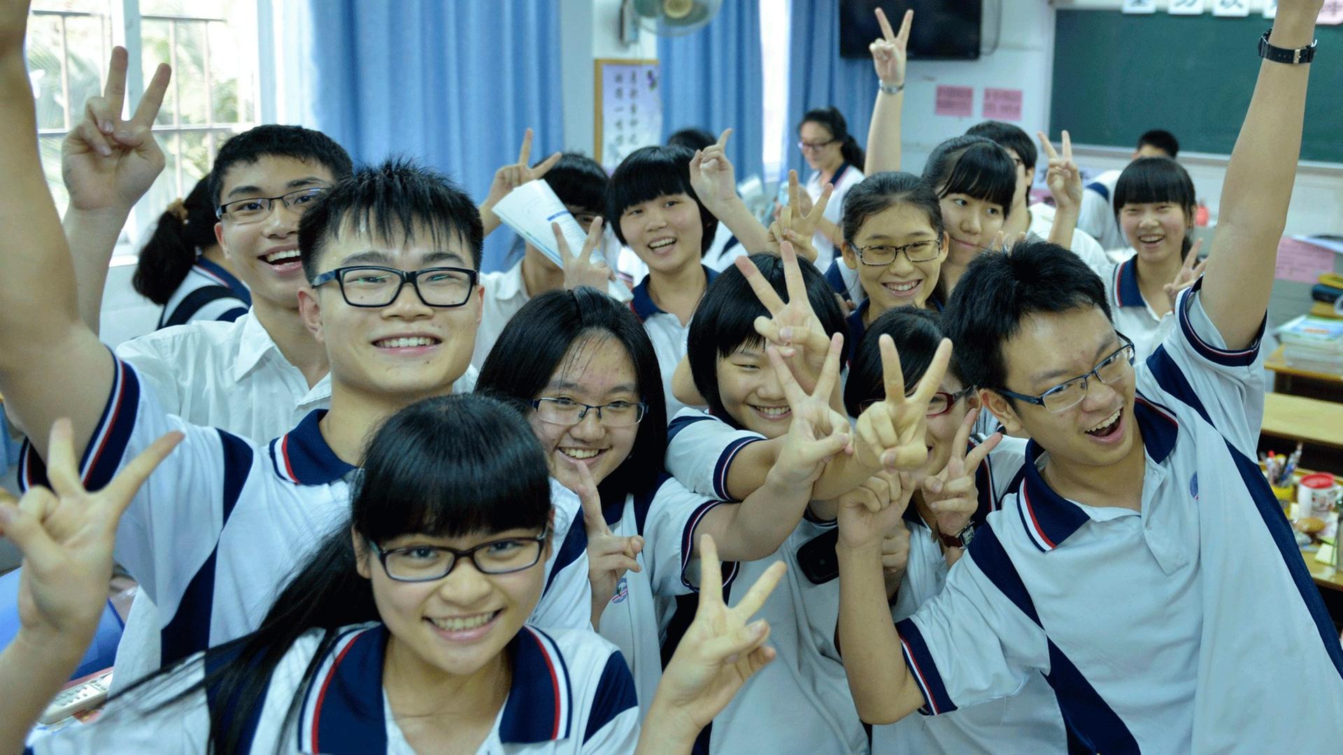 Eine chinesische Schülergruppe in Guangzhou, die ihre bestandene Aufnahmeprüfung für die Uni feiert. Die Schüler tragen kurzärmelige Uniformen und machen das Peace-Zeichen.