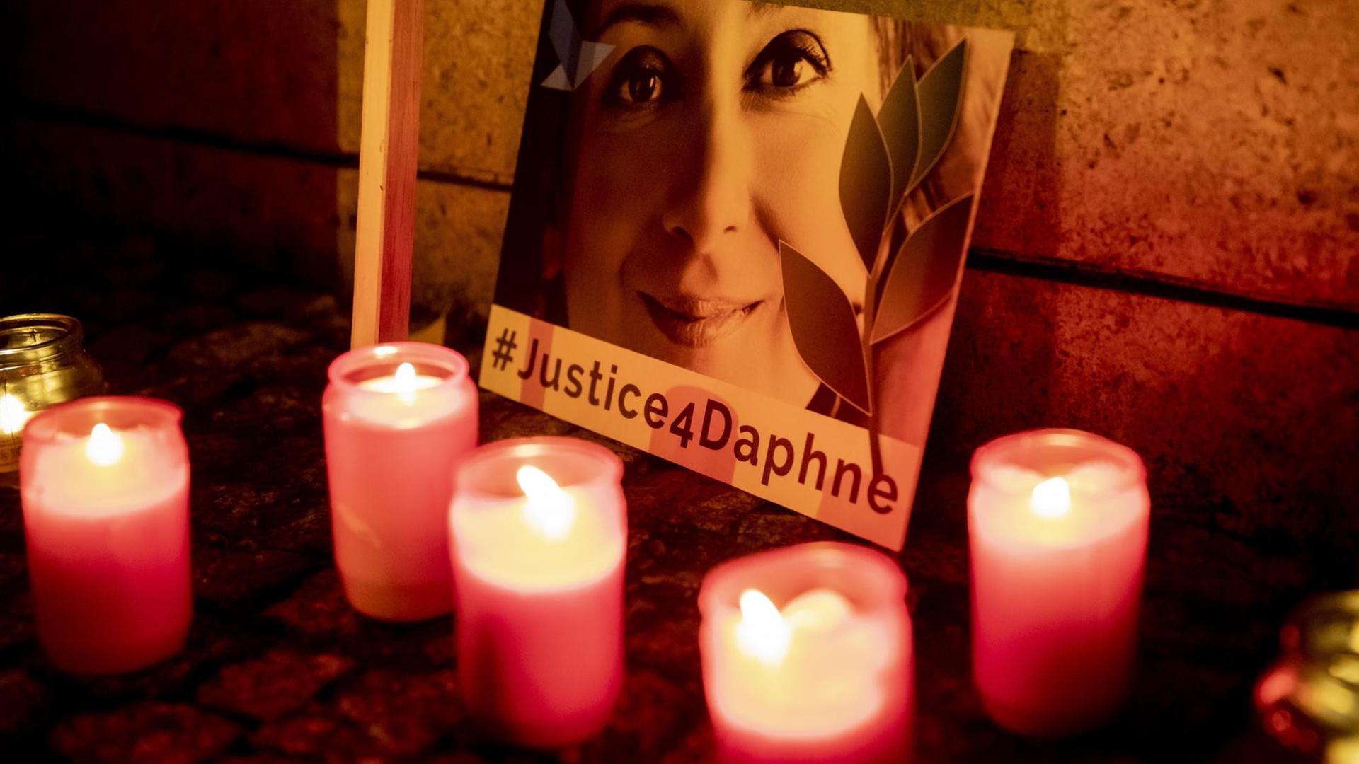 Mehrere Grabkerzen stehen vor einem Bild der maltesischen Investigativjournalistin Daphne Caruana Galizia. Darauf die Aufschrift: #Justice4Daphne.