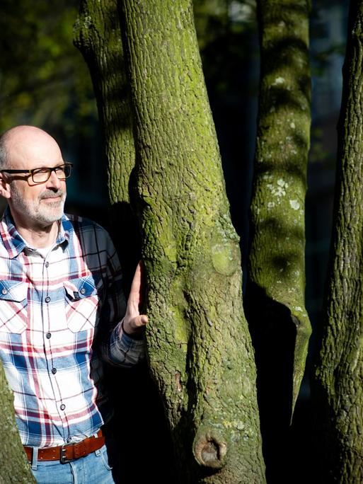 Das Foto zeigt den Förster und Bestseller-Autor Peter Wohlleben, wie er zwischen zwei Bäumen steht.