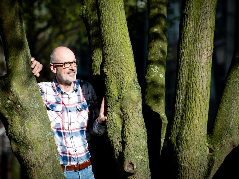 Das Foto zeigt den Förster und Bestseller-Autor Peter Wohlleben, wie er zwischen zwei Bäumen steht.