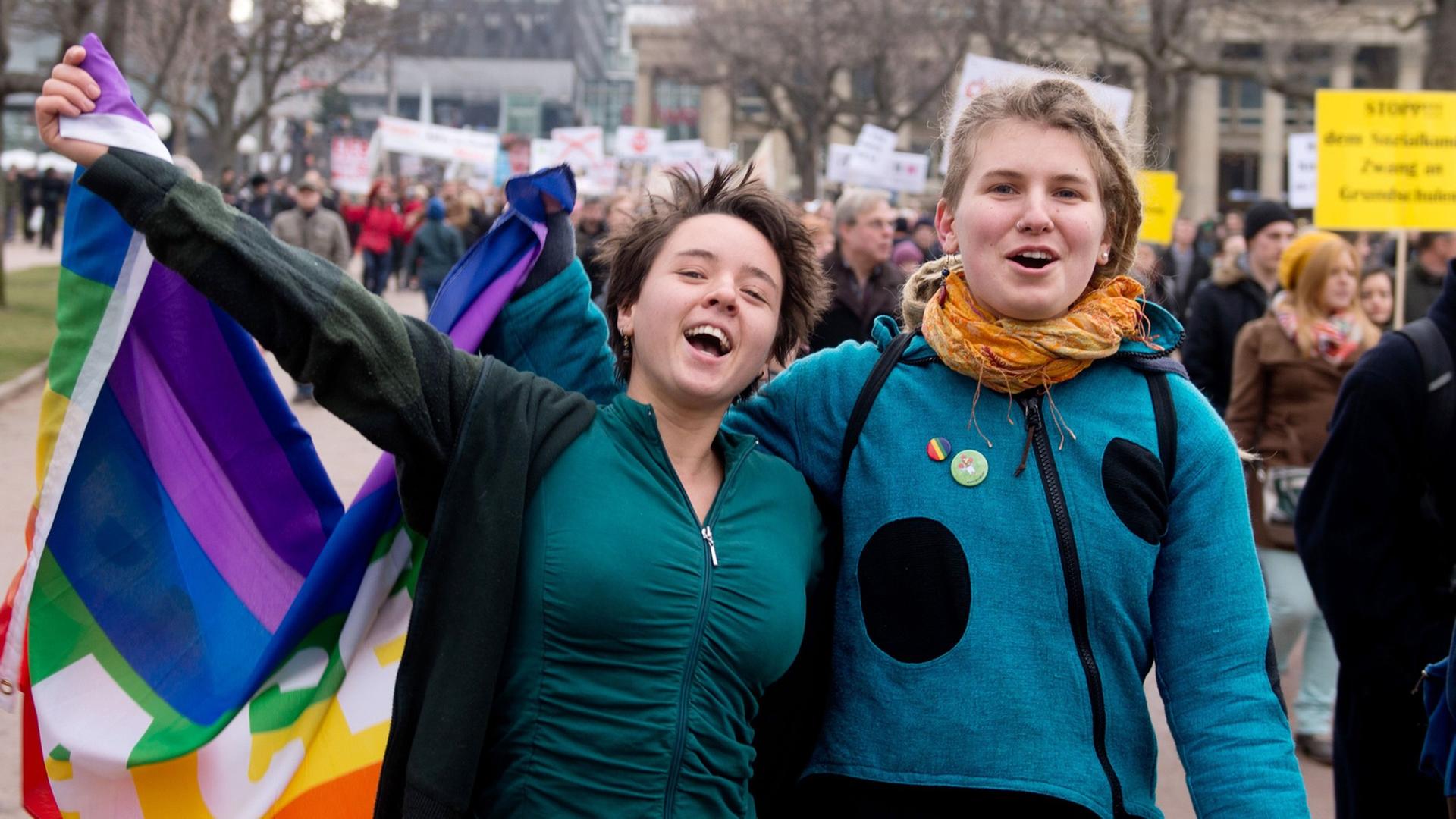 Zwei Befürworter der Aufwertung des Themas Homosexualität im Schulunterricht in Baden-Württemberg gehen am 01.02.2014 bei einer Demonstration in Stuttgart (Baden-Württemberg) über den Schlossplatz, in der Hand eine Regenbogenfahne.